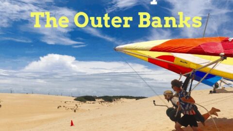People hang gliding on sand dunes under a blue sky with text overlay.
