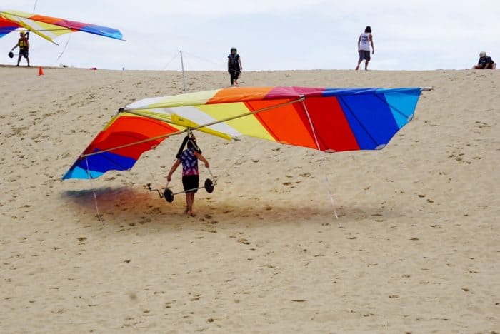 instructor carryin hang glider up sand dune